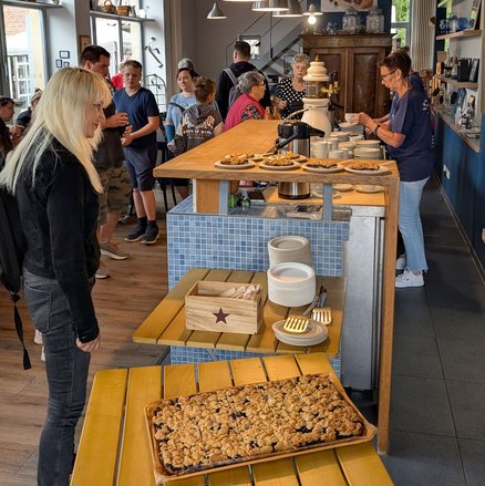 zeigt Blick in die Blaubeerscheune mit Blaubeerkuchen im Vordergrund und sich dort aufhaltenden Personen