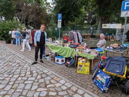 zeigt mehrere Ausstellungsstände für Bekleidung und Spielzeug auf einer Pflasterfläche und verschiedene Personen