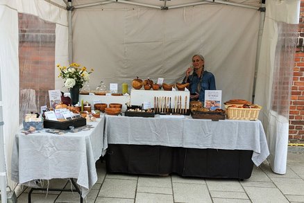 zeigt Marktstand mit gedrechselten Produkten und die Anbieterin