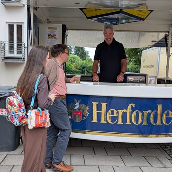 zeigt Getränkestand mit Person, die ausschenkt und Kunden