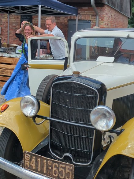 zeigt Oldtimer und 2 Personen, die gerade aussteigen