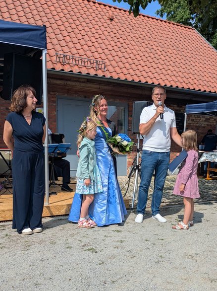 zeigt eine Personengruppe aus 3 Erwachsenen und 2 Kindern, wobei der Mann ins Mikrofon spricht