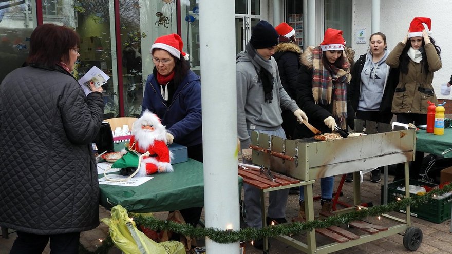 öffnet internen Link in aktuellem Fenster zeigt weihnachtlich kostümierte Kinder und Erwachsene an Markt- und Grillständen vor einem Gebäude