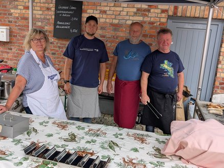 zeigt 4 Personen hinter einem Grillstand
