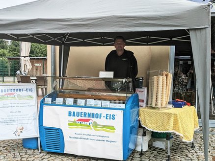 zeigt Marktstand, der Bauernhof-Eis anbietet und einen Mann hinter dem Stand